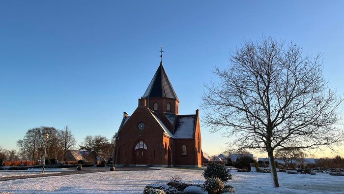 En rød kirke med spiret og klokke i en snedækked park