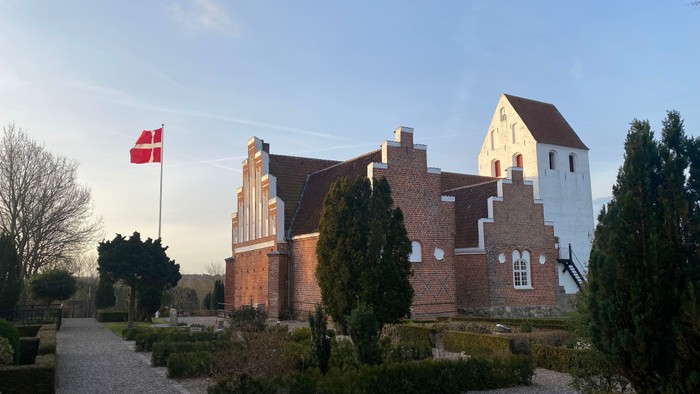 En rød murstenskirke med dansk flag på en klar dag