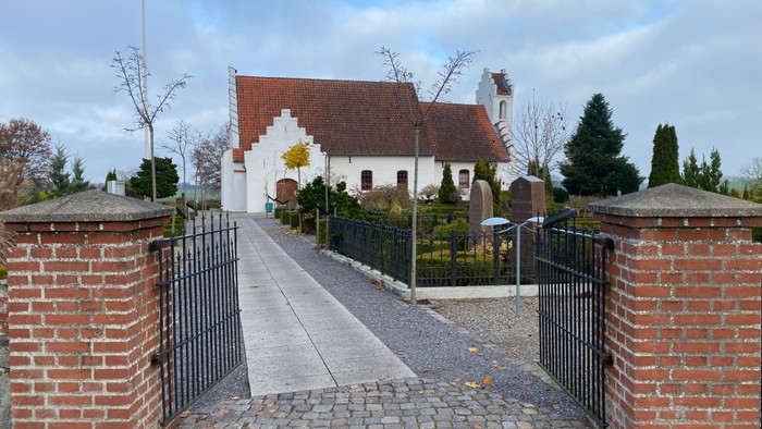 En smuk kirke med røde tag og hvidt udseende, omgivet af en mur og en sti.
