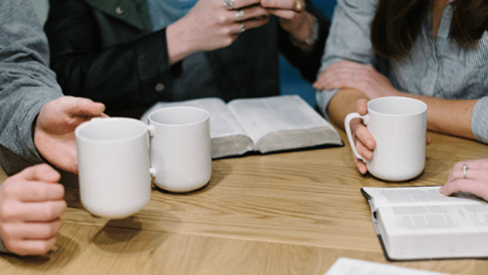 En gruppe af mennesker sidder ved et bord med kaffe og bibler.