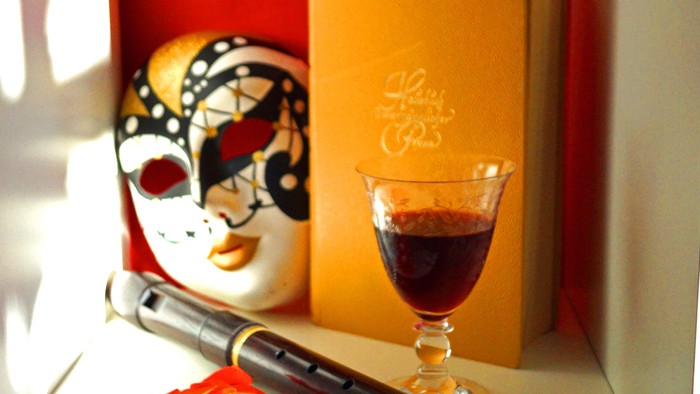 Ein Maskenbild, eine Flöte und ein Weinglas auf einem Tisch