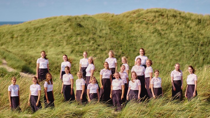 En gruppe unge kvinder i matchende tøj poser sammen på en græsklædt bakkeside.