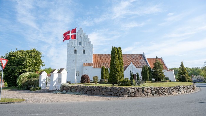 En hvid kærmisk tårn med rødt tag og dansk flag på en stenmur ved en vej