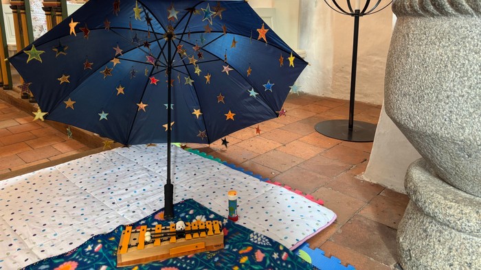 En blå paraply med stjernemønstre er udstillet indendørs ved siden af en stor stenvaske og et bord med et farverigt borddug.