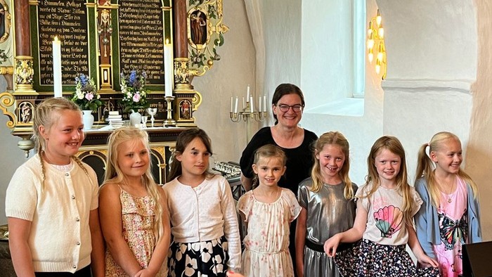 En gruppe børn og en kvinde står i en kirke foran et orgel