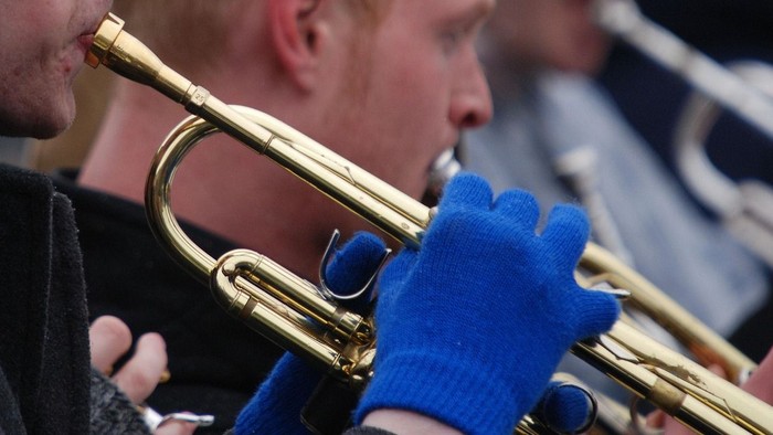 Musiker, der Trompete spielt und dabei blaue Handschuhe trägt.