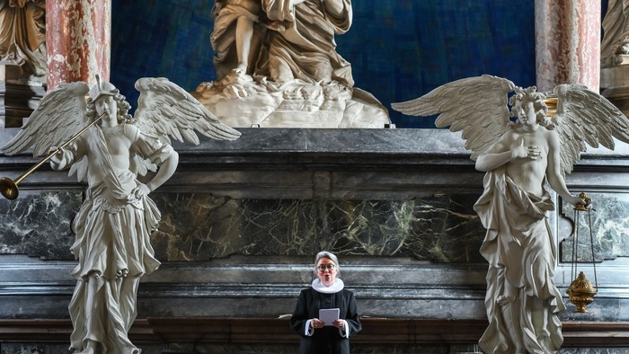 En præst står i en prægtig kirke med store skulpturer og malerier.