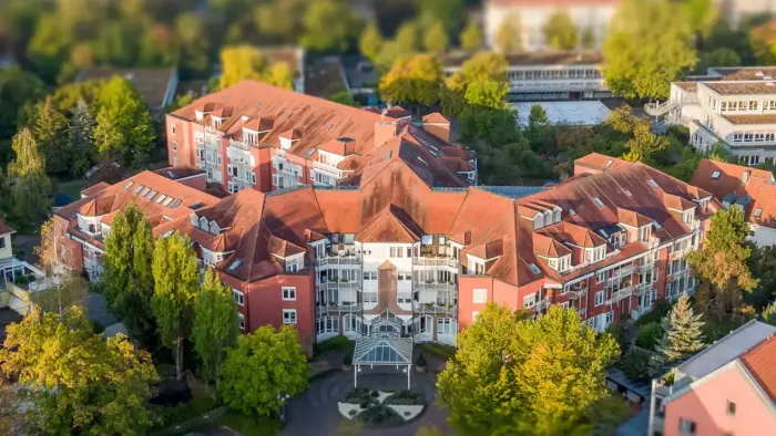 Luftaufnahme eines Wohngebiets mit rotbedachten Gebäuden und üppig grünen Bäumen.