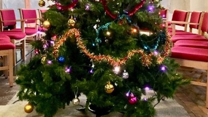 Christmas tree decorated with colorful ornaments and lights in a church setting