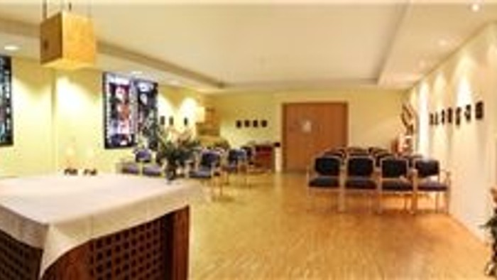 Großes Wohnzimmer mit Holzböden, weißen Wänden und moderner Einrichtung, darunter ein weißes Sofa, ein Couchtisch und zwei Sessel. An den Wänden hängen zwei große Gemälde, und von der Decke hängt ein Kronleuchter.