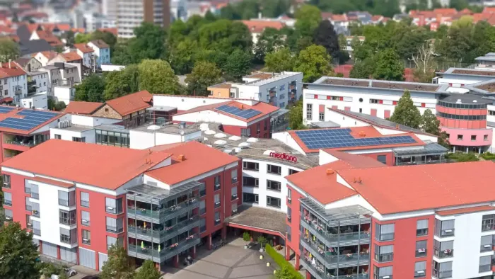 Luftaufnahme einer Stadt mit rotbedachten Gebäuden und umgebendem Grün