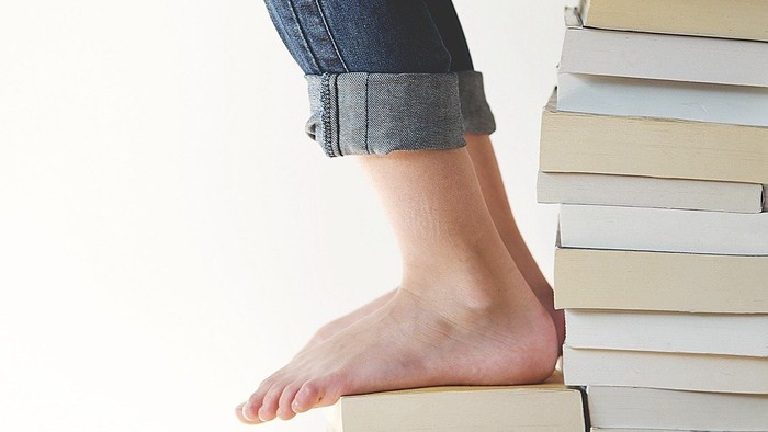 En person sidder på en høj stabel bøger.