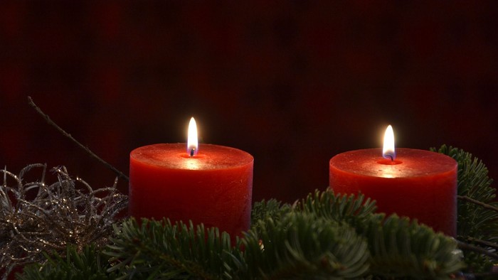 Zwei brennende rote Kerzen auf grünem Tannengrün