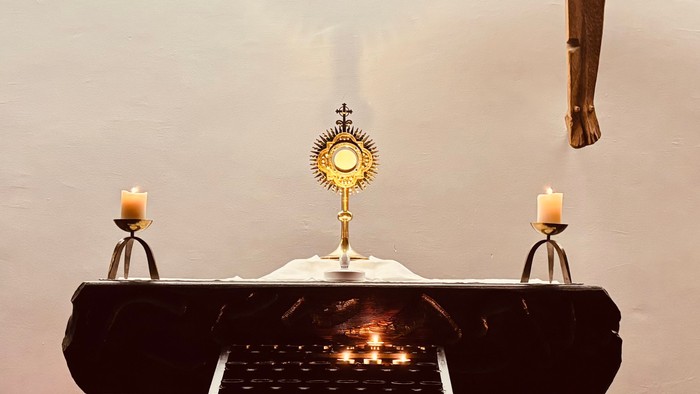 Ein Altar in einer Kirche mit Kerzen, Blumen und einer hängenden Holzskulptur.