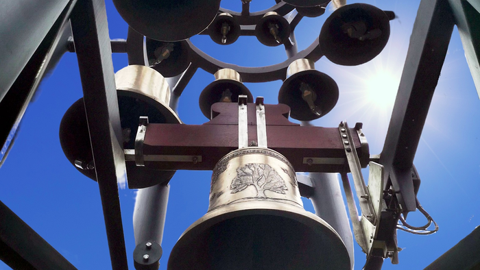 Nahaufnahme einer großen Glocke, die in einem metallenen Glockenturmgerüst vor klarem Himmel hängt.