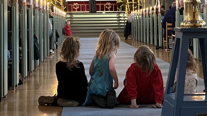 Tre børn sidder i en kirke.