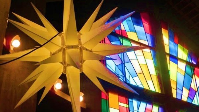 Leuchtende Papiersterne vor buntem Kirchenfenster