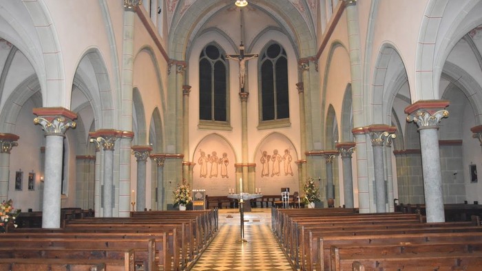 Innenraum einer Kirche mit hölzernen Bänken und hohen Fenstern