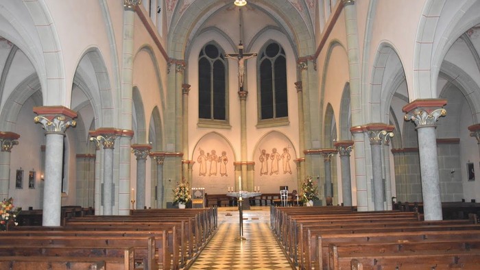 Innenraum einer Kirche mit hölzernen Bänken und hohen Fenstern