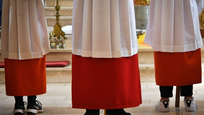 Drei Priester in roten und weißen Gewändern stehen in einer Kirche.