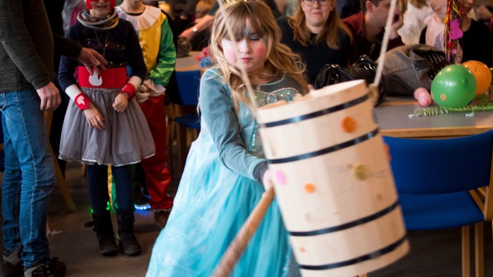 En pige i blå kagepølde og kronet spiller med en kæmpe pinde og bolle.