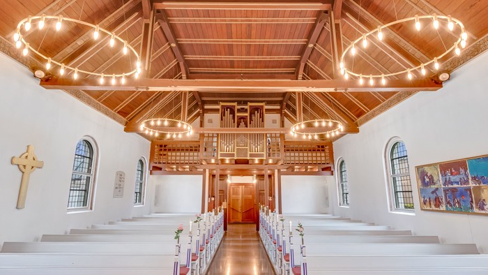 Indre del af en kirke med hvidt indvendigt og trædekkede lofter.