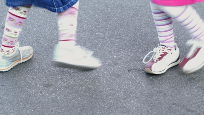 Zwei Kinder laufen mit bunten Socken und weißen Schuhen auf Asphalt.