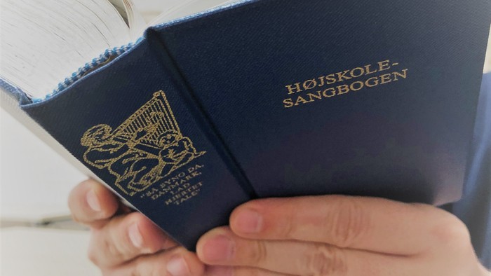 Hånd holder blå bog med guldindskrift 