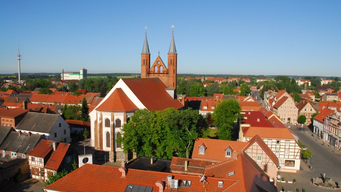 Die Stadtansicht zeigt eine Kirche mit zwei Türmen und rote Dächer.