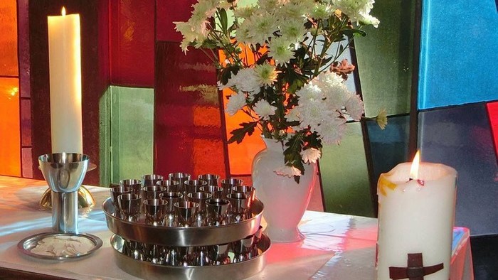 Buntes Kirchenfenster mit Kerzen, Blumen und Kreuz.