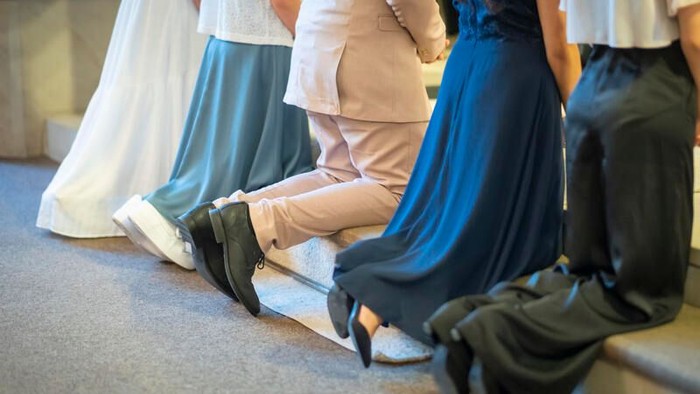 Eine Gruppe von Personen in formeller Kleidung, darunter Hochzeitskleider und Anzüge, die eng beieinander in einem Innenraum sitzen.