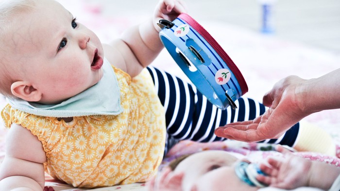 Et spæd barn ligger på ryggen og holder en børnetoy i hånden.