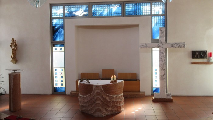 Ein runder Altar mit zwei brennenden Kerzen vor einem großen Kreuz aus Marmor.
