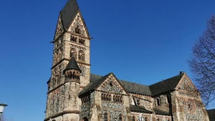 Gotische Kirche mit hohem Turm und filigranen Details vor blauem Himmel