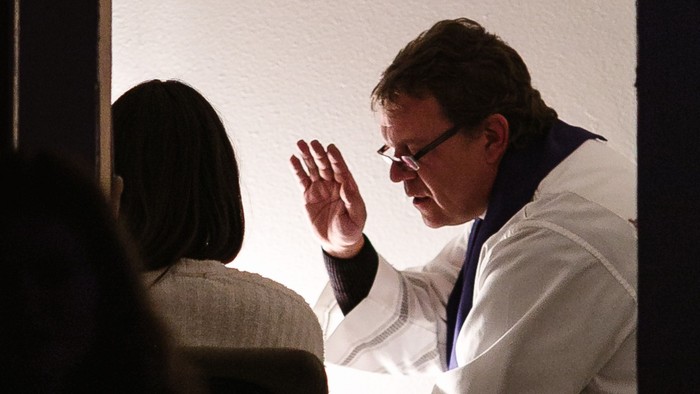 Ein Mann in weißem Anzug winkt auf einer Bühne.