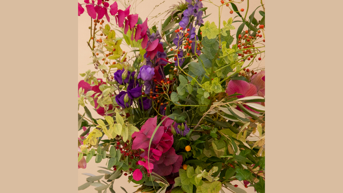 Farverigt buket med lilla, lyserøde og røde blomster samt frodigt grønt løv i en naturlig sammensætning.