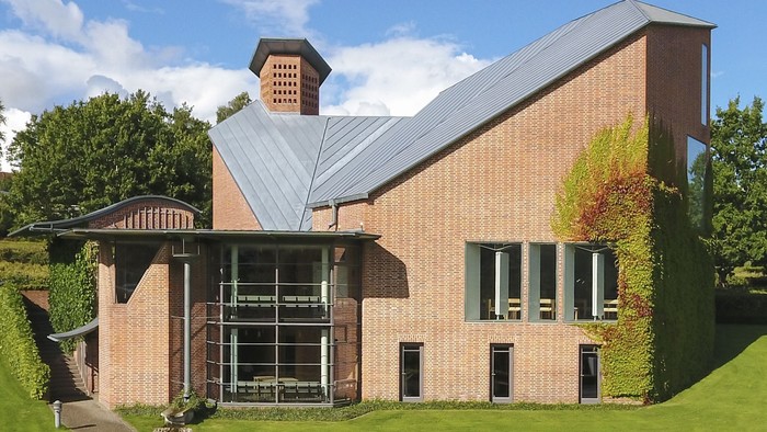 Moderne murstensbygning med mure dækket af vedbend, store glaspartier og et skråt metal-tag.