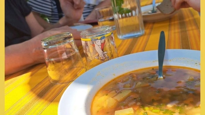 Menschen genießen eine herzhafte Suppe im Freien an einem bunten Tisch mit Getränken in der Nähe.