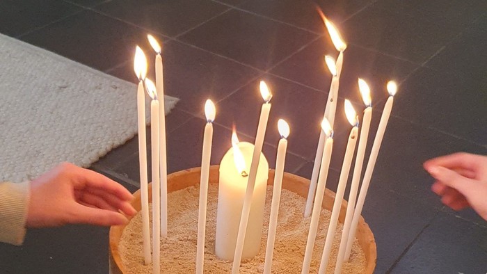 Ein Kerzenhalter mit mehreren brennenden Kerzen, die in einem kreisförmigen Muster auf einer strukturierten Basis angeordnet sind.