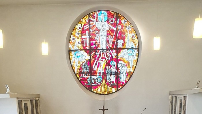 Elegante Kircheninnenausstattung mit einem lebendigen Buntglasfenster über einem schlichten Altar mit Kerzen und Blumenschmuck.
