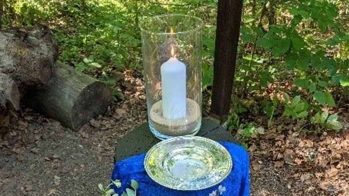 Ein ruhiger Outdoor-Altar mit Blumen, einer brennenden Kerze und einem offenen Buch auf blauem Tuch.