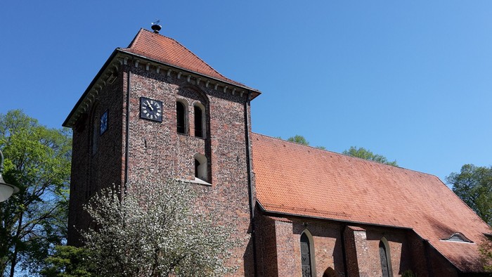 Das Bild zeigt eine alte Kirche mit einem hohen Turm und einem Ziegeldach.