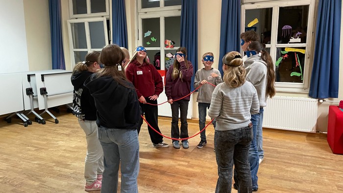 Eine Gruppe von Menschen, die in einem hell erleuchteten Raum ein Indoor-Spiel mit Leuchtarmbändern spielen.