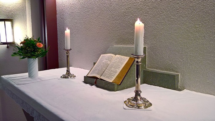 Ein Tisch mit brennenden Kerzen, einer Bibel und einer Vase mit Blumen