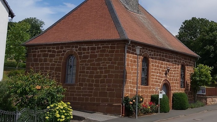 Kleine Backsteinkirche mit rotem Dach und Glockenturm.