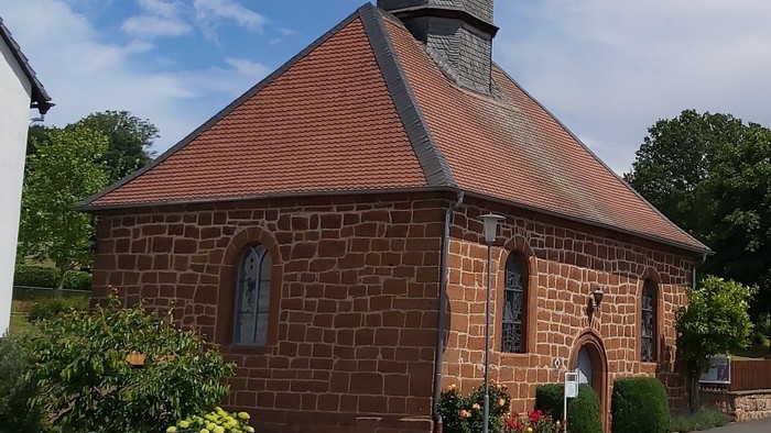 Kleine Backsteinkirche mit rotem Dach und Glockenturm.