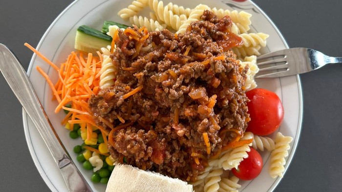 En tallerken med pasta, kødsauce og grøntsager. 