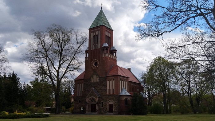 Ein rotes Ziegelgebäude mit grünem Dach und Uhrturm in einem Park