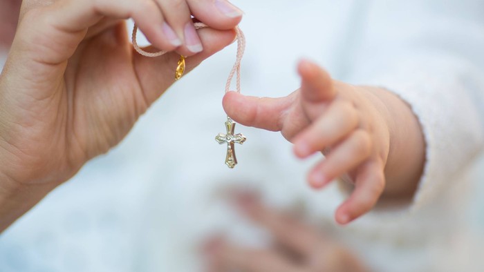 En person holder en guld crucifaks med en småhånd i baggrunden