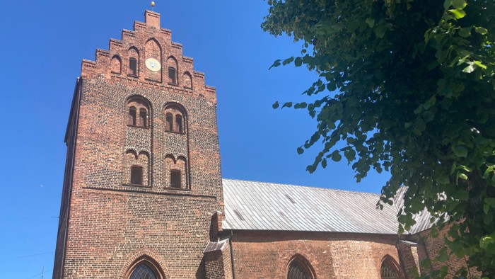 Røde murstenskirke med tårn og spids tak.